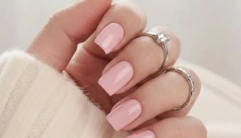En hand med naglar målade i mjukt nagellack rosa, prydd med två silverringar.