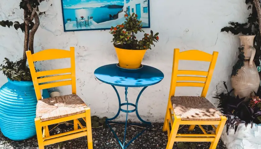 Zwei gelbe Stühle und ein blauer Tisch mit Blumentopf. Ein Bild mit Meerblick hängt an der Wand. Hier sind die Kos Geheimtipps für dein nächstes Foto!