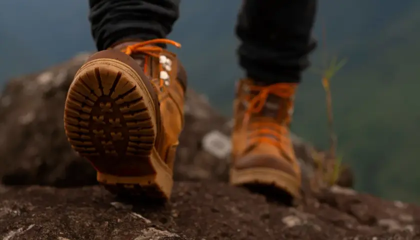 Stopy w brązowych butach trekkingowych z pomarańczowymi sznurówkami stąpają po kamieniach. W butach zastosowano membranę, chroniącą przed wilgocią.