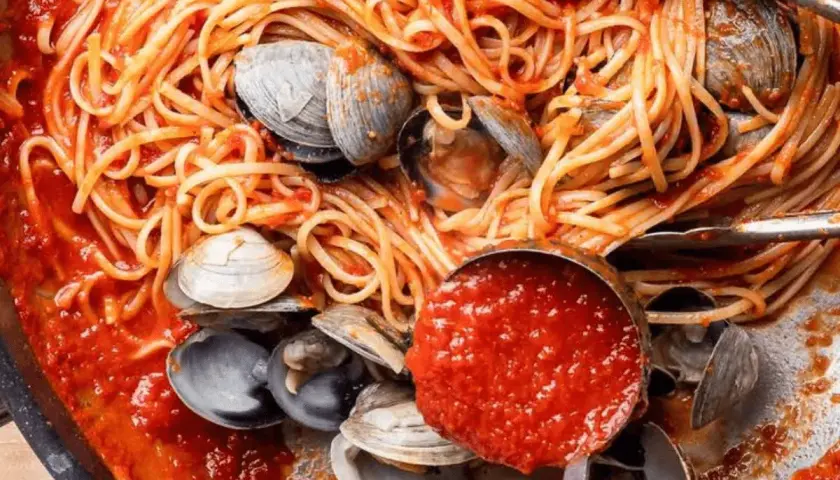Spaghetti alle vongole, un plat de pâtes aux palourdes et sauce tomate, servi dans une poêle avec une louche de sauce.
