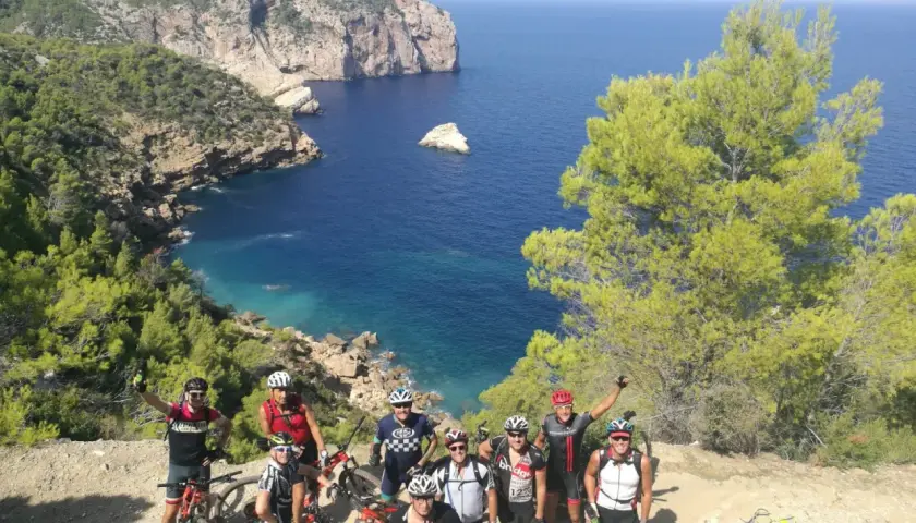 Grupo de ciclistas posa con sus bicicletas en un acantilado con vistas al mar azul. ¡Una aventura en la bicicleta Ibiza!