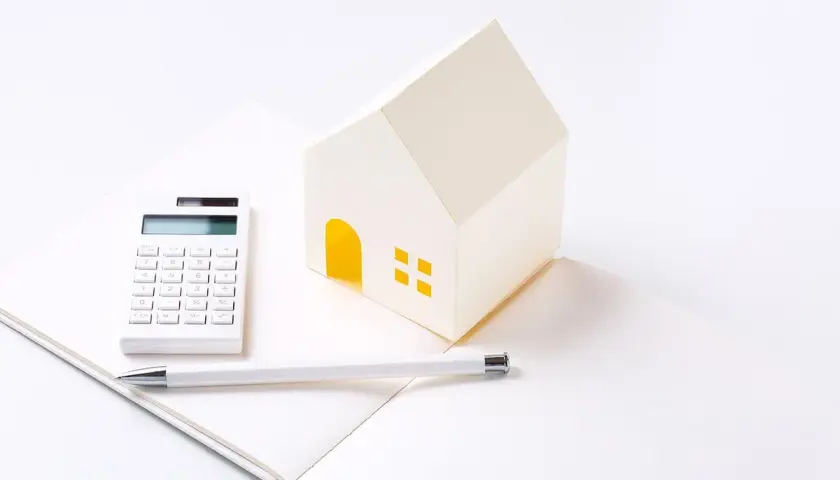 Maison en papier, calculatrice et stylo sur un carnet ouvert, symbolisant les **PTZ travaux soi-même**.