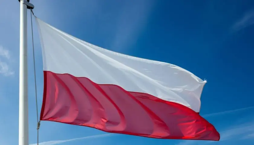 Polska flaga powiewa na maszcie na tle błękitnego nieba.
