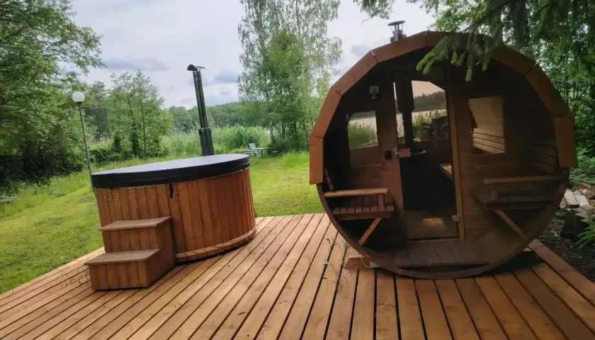 Drewniany domek z jacuzzi i sauną na wyłączność, otoczony zielenią, z widokiem na jezioro. Idealne miejsce na relaks.