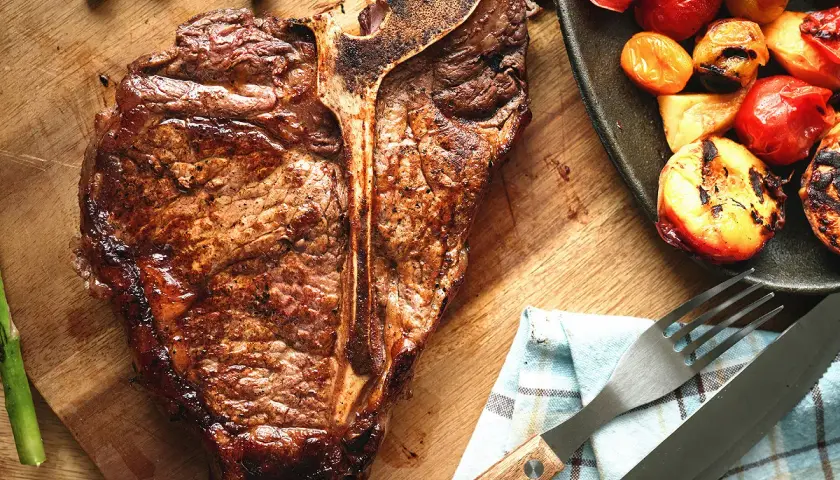 Une côte de bœuf juteuse, accompagnée d'asperges et de tomates grillées, prête à être dégustée.