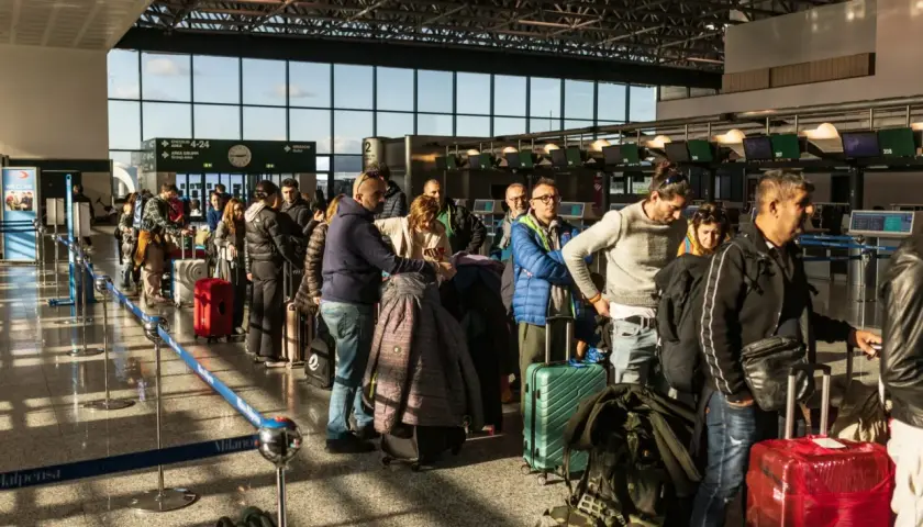 Kolejka pasażerów z bagażami na lotnisku we Włoszech. W tle widać stanowiska odprawy.