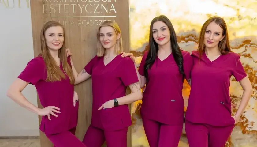 Cztery kobiety w uniformach medycznych stoją obok siebie przed tablicą z napisem "Kosmetologia Estetyczna".