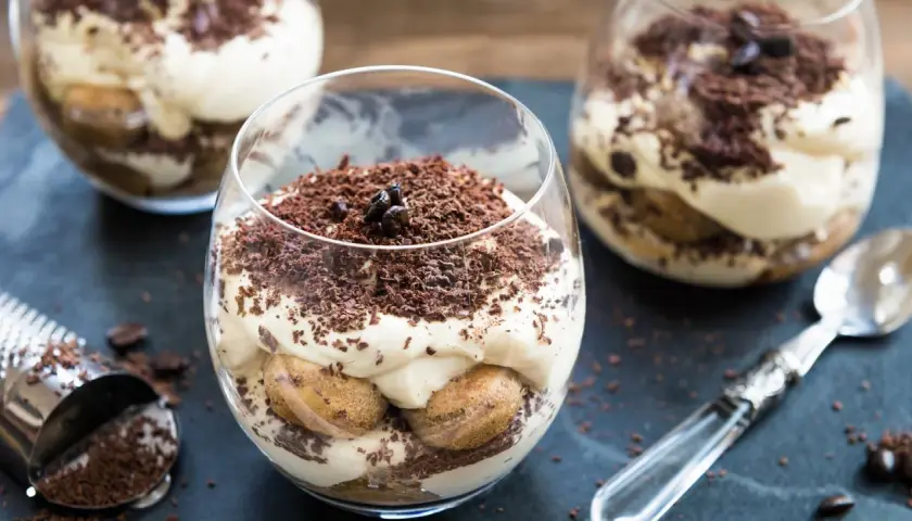 Deser tiramisu w szklance, posypany startą czekoladą i ziarnami kawy.