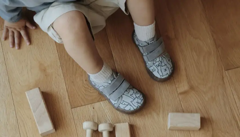 Roczne dziecko bawi się drewnianymi klockami na podłodze. Ma na sobie kapcie w kotki, idealne do chodzenia po domu.