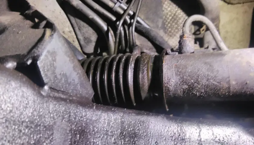 Zbliżenie na skorodowaną maglownicę samochodową z widocznymi przewodami hydraulicznymi.