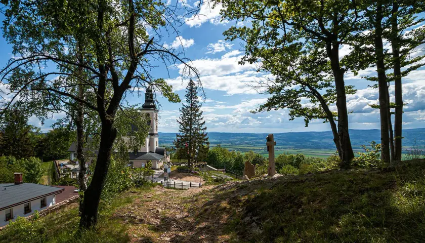 Widok na kościół i krzyż na wzgórzu w **śnieżnicki park krajobrazowy**. W oddali rozciąga się malownicza dolina.