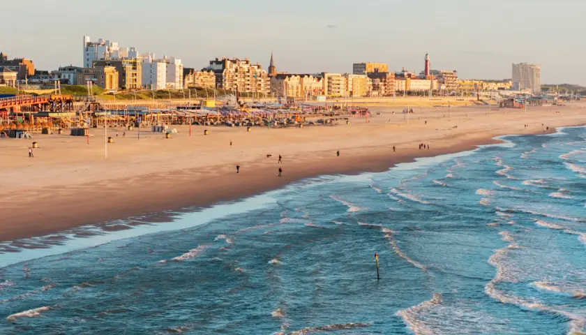 Ein sonniger Tag am **niederlande strand** mit Wellen, Sand und einer Stadtkulisse im Hintergrund.