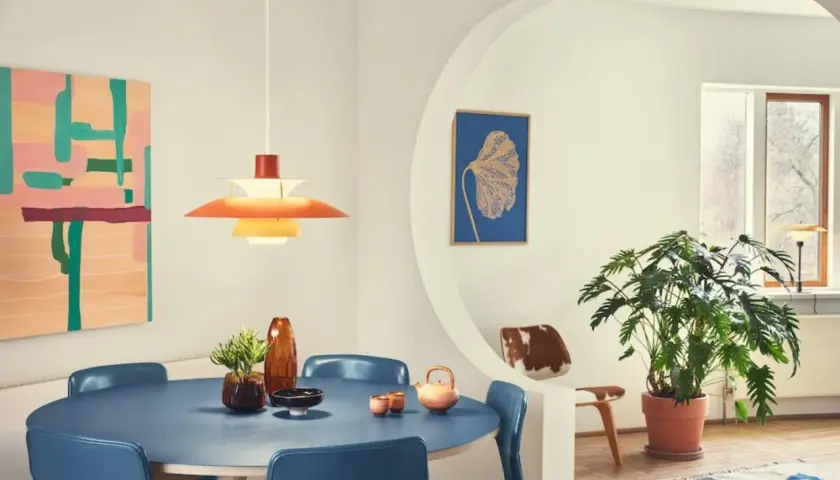 Ein Esszimmer im **midcentury modern** Stil mit blauem Tisch, blauen Stühlen, einer bunten Wandkunst und einer markanten Hängeleuchte.