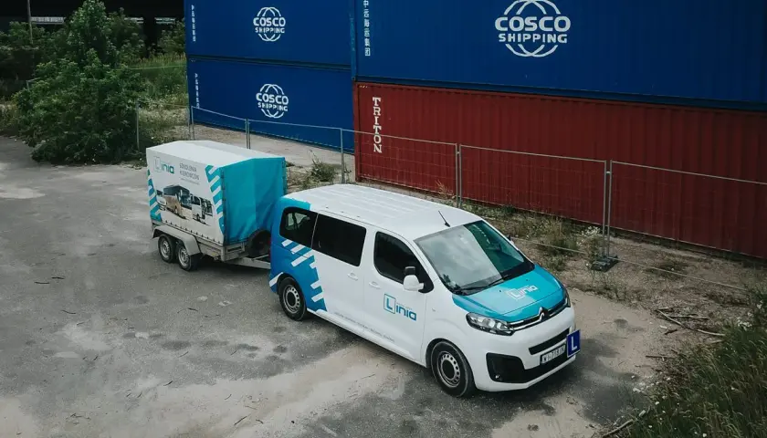 Biały bus z przyczepą, oznakowany logo "Linia", stoi obok kontenerów. To może być szkolenie, gdzie poznasz prawo jazdy b+e koszt.