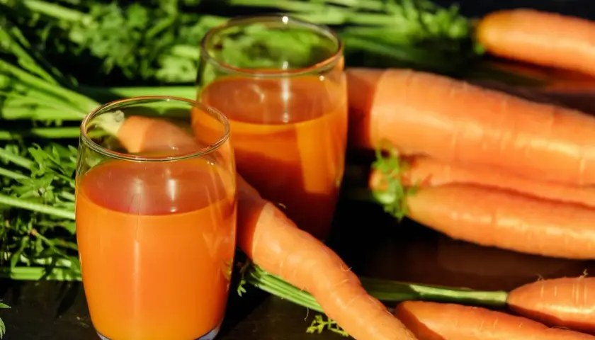 Frischer Karottensaft in Gläsern, umgeben von ganzen Karotten. Ein tolles Beispiel für vitamin a welche lebensmittel.