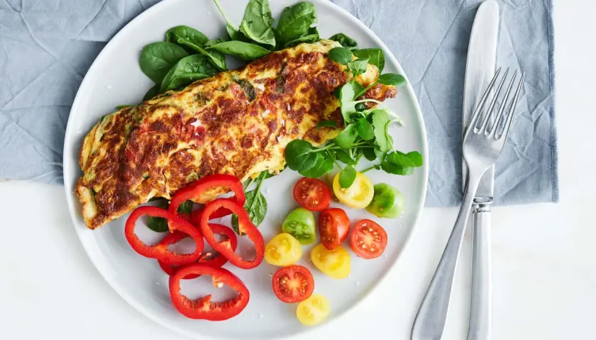 En gyllene, nyttig omelett serverad med färska grönsaker som spenat, körsbärstomater och paprika. En perfekt start på dagen!