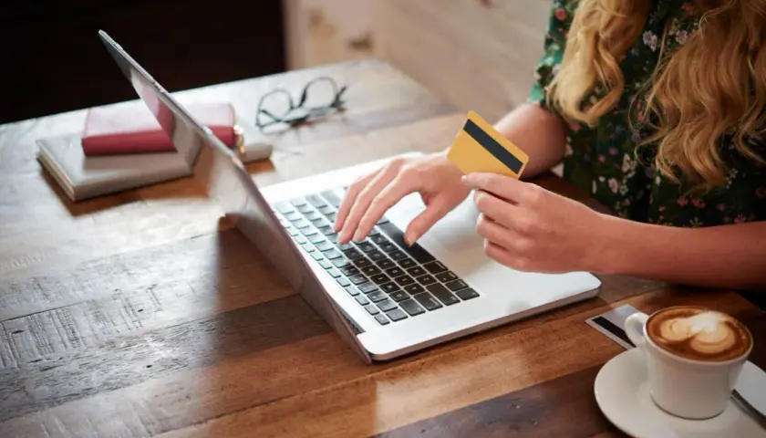 Kobieta z kartą płatniczą na laptopie, szukająca pożyczki dla każdego bez odmowy. Kawa obok.