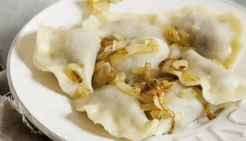 Pyszne pierogi z kapustą i skwarkami, ułożone na białym talerzu, kuszą swoim domowym wyglądem.
