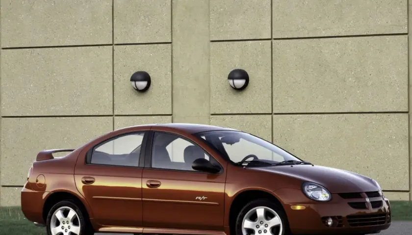 Brązowy Dodge Neon R/T z 2004 roku stoi przed betonową ścianą z dwoma okrągłymi lampami.