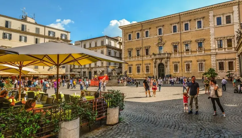 Piazza animata con gente che passeggia e si gode la movida a Roma, tavolini all'aperto e palazzi storici sullo sfondo.
