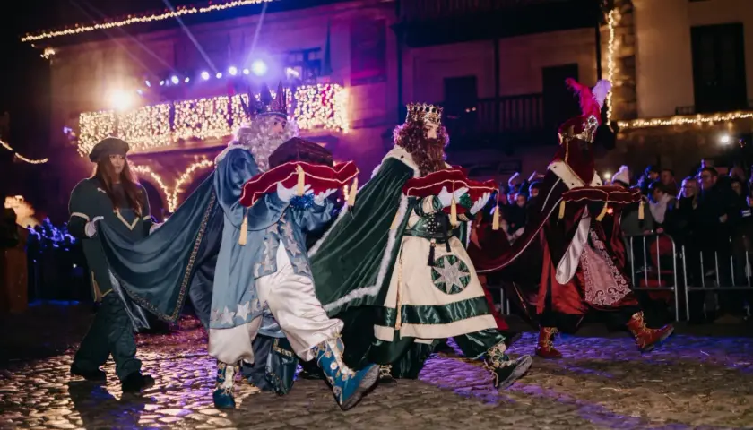 Los Reyes Magos desfilan en la cabalgata de Santillana del Mar, portando regalos bajo luces festivas.