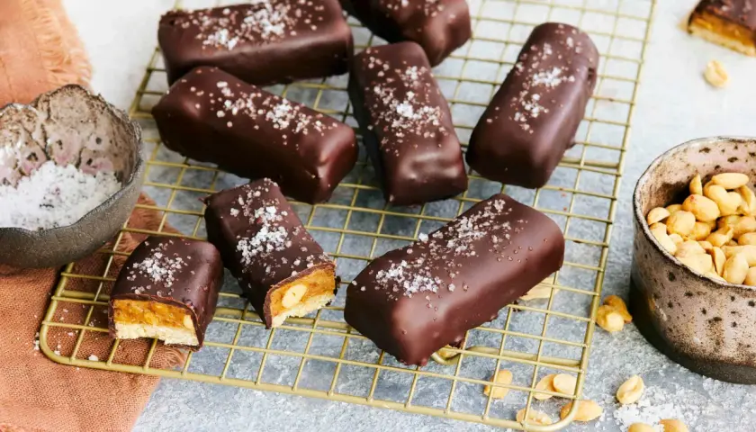 Vegane Snickers mit Karamell, Erdnüssen und Meersalz bestreut, auf einem goldenen Gitter.