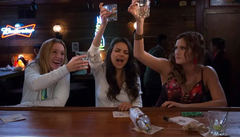 Tre kvinnor skålar glatt vid en bardisk, en scen från rollistan i Bad Moms.