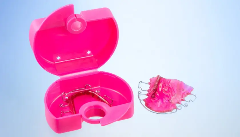 Caja ortodoncia rosa abierta con un retenedor dentro y otro fuera.
