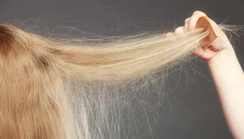 En hand håller en träkam genom blont, tunt hår. Håret ser lite slitet ut, inte krusigt.