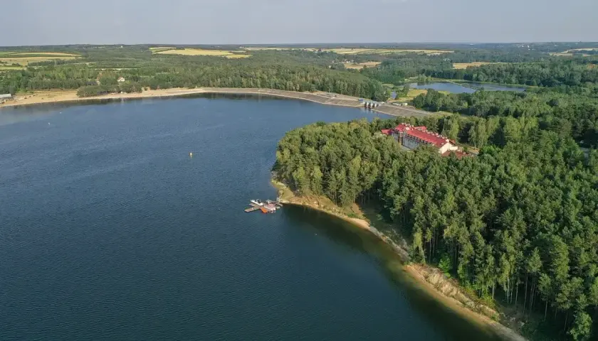 Malownicze jezioro Chańcza otoczone lasem, z hotelem i pomostem.