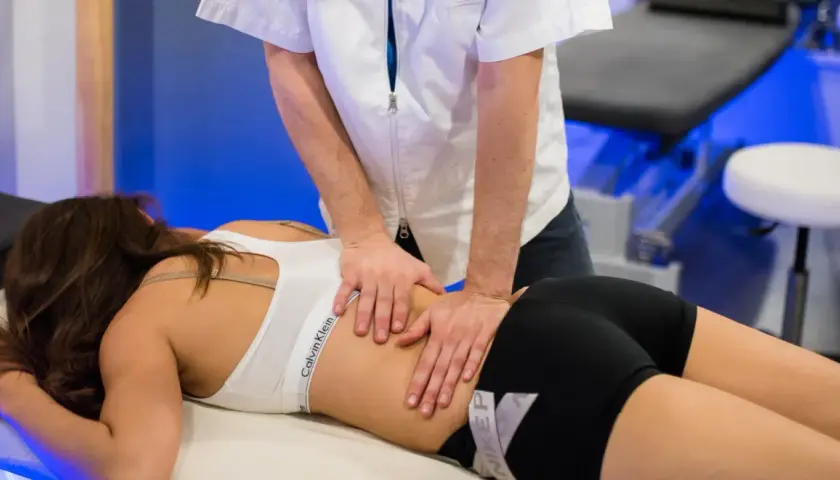 Un professionnel effectue un massage musculaire sportif sur le dos d'une femme allongée sur une table de massage.
