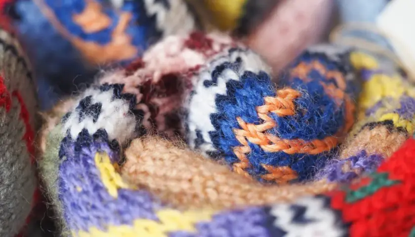 Gros plan sur un tissu jacquard aux motifs géométriques colorés, avec des fils de laine bleus, violets, jaunes et rouges entrelacés.