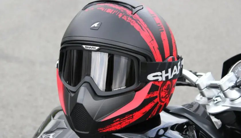 La calotta del casco Shark, nera con grafiche rosse a strisce e un sole nascente, è pronta per l'avventura.