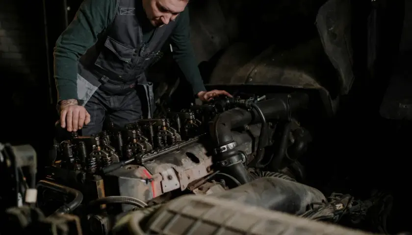 Mechanik w kamizelce pracuje nad silnikiem, wykonując odpowietrzanie silnika.