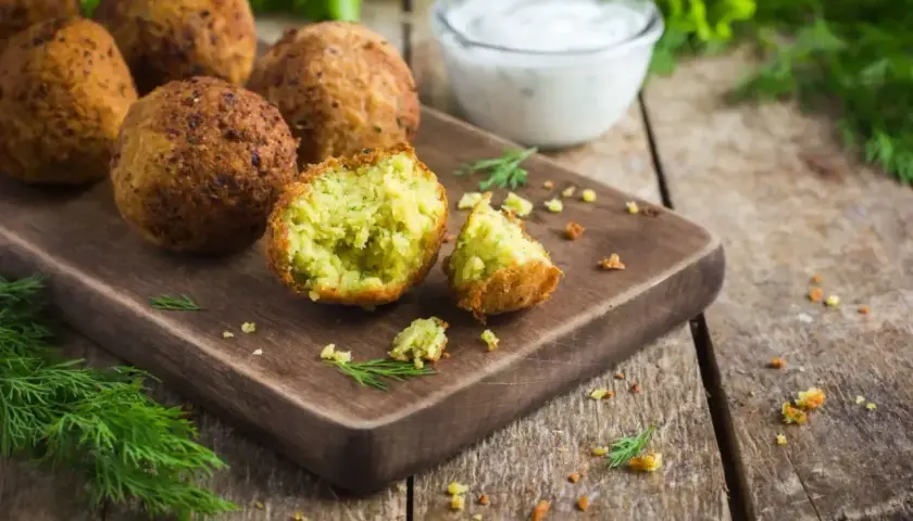 Chrupiące falafel na desce, jeden przekrojony, z sosem jogurtowym i koperkiem. Idealny falafel przepis.