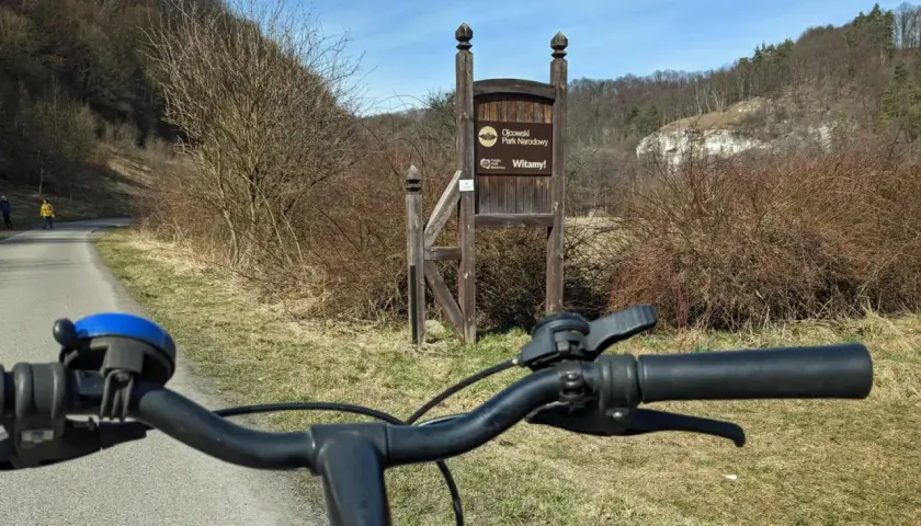 Rowerem przez Ojcowski Park Narodowy. Wita nas drewniany drogowskaz i malownicze wapienne skały w tle.