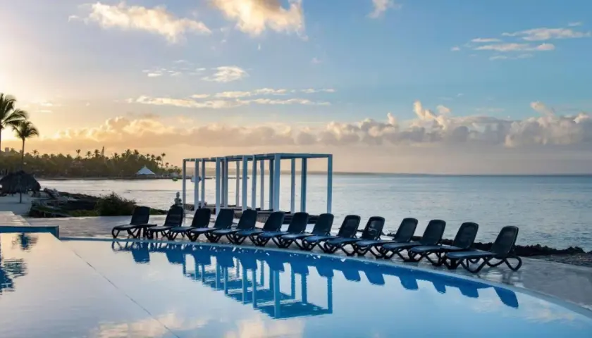 Słońce wschodzi nad Viva Dominicus Beach by Wyndham. Leżaki czekają nad basenem z widokiem na ocean i palmowe wybrzeże.