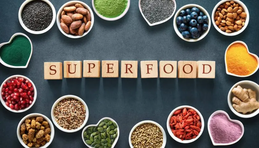 Scopri quali sono i superfood: semi di chia, mirtilli, mandorle, curcuma, zenzero, bacche di goji e altro ancora, disposti attorno alla parola "SUPERFOOD".