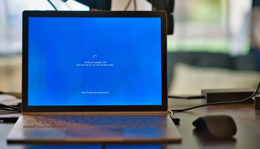 Laptop z niebieskim ekranem Windows, na którym trwa aktualizacja. Proces "Windows Modules Installer Worker" jest w toku, postęp 27%.