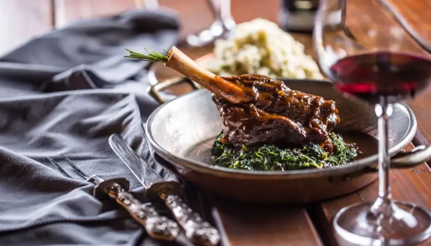 Un plat de vin avec agneau, servi sur un lit d'épinards, avec une branche de romarin. Un verre de vin rouge est à côté.