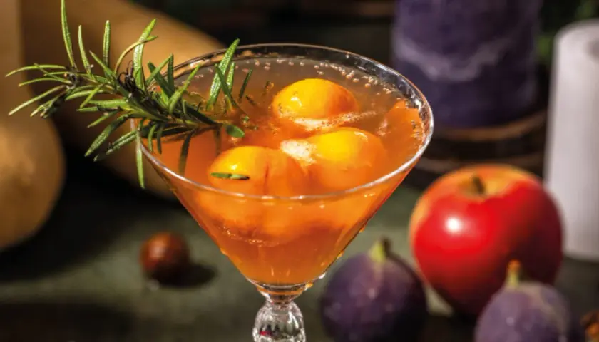 Cocktail fruité avec des pêches et du romarin, parfait pour une idée apéro mariage. Pomme et figues en arrière-plan.