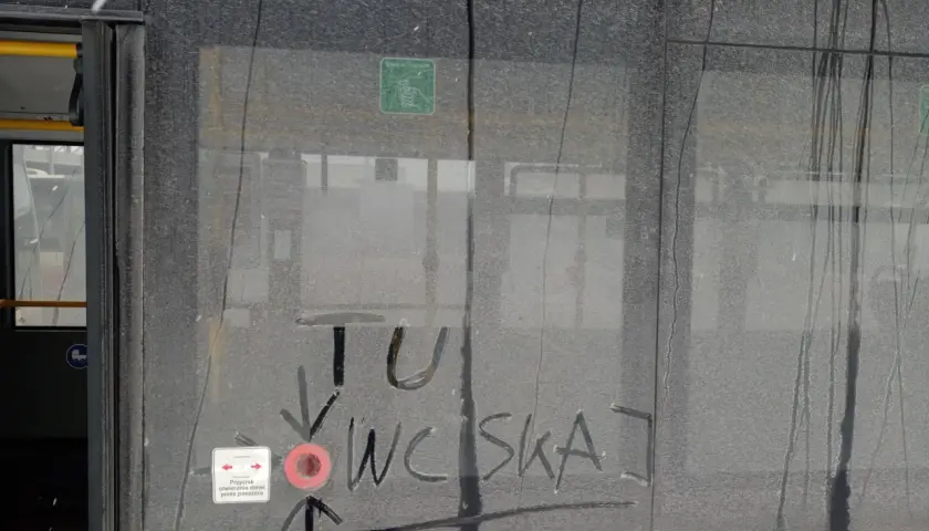 Brudne drzwi pociągu z napisem "TU WCISKAJ" i ikoną przycisku otwierania drzwi.