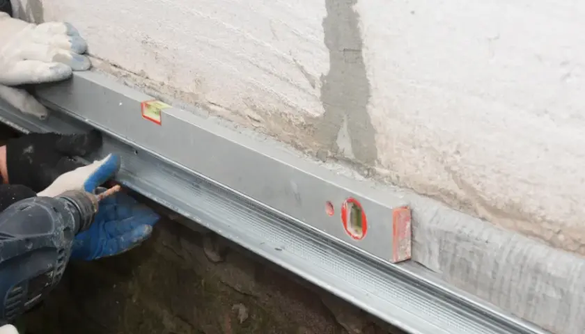 Handwerker montieren mit Wasserwaage und Bohrmaschine eine Horizontalsperre aus Blech an einer Wand.