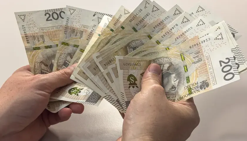 Dwie ręce trzymają wachlarz banknotów po 200 złotych. Czy to duł, czy dół, ważne, że pieniądze są!