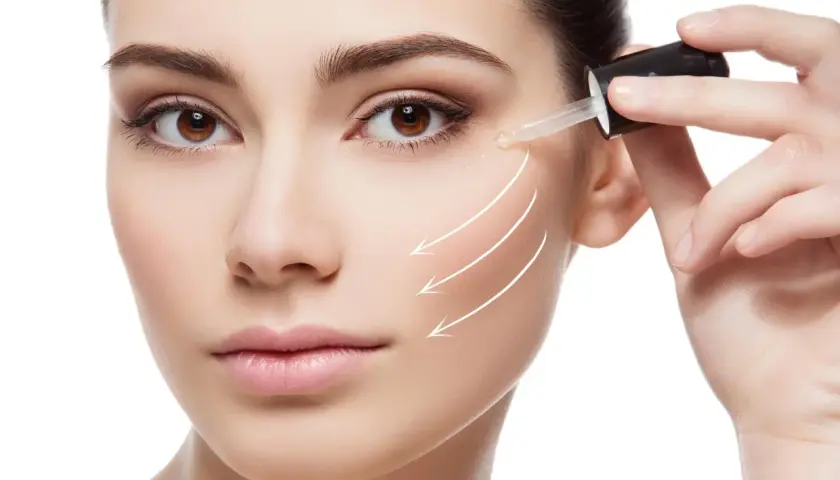 Kobieta aplikuje serum na twarz z pipetki, widoczne białe linie wskazujące na poprawę skóry.