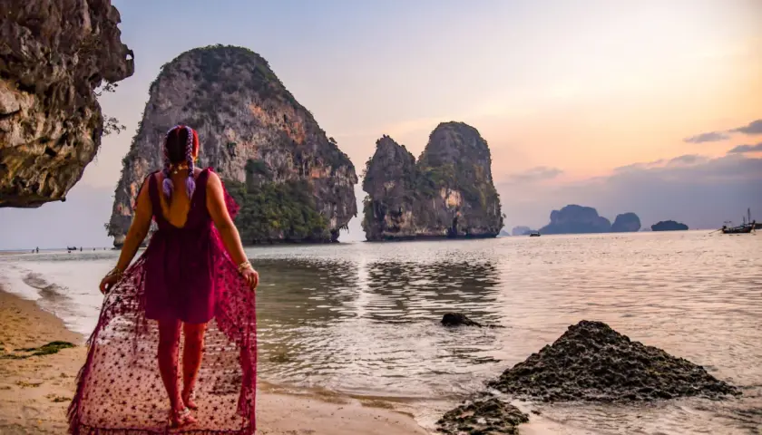 Kobieta w zwiewnej sukience spaceruje po plaży Ao Nang, podziwiając skaliste wysepki o zachodzie słońca.
