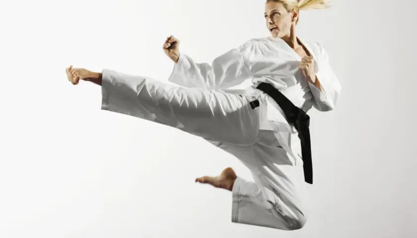 Kobieta w białym karate gi wykonuje wysokie kopnięcie w powietrzu.