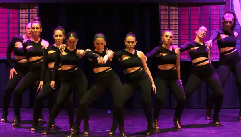 Un gruppo di ballerine in abiti neri si esibisce su un palco illuminato, creando un'atmosfera da dance hall.