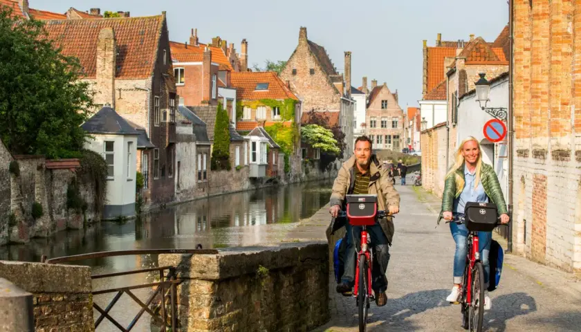 Couple enjoying a Bruges bike tour along a canal, with historic buildings lining the waterway.