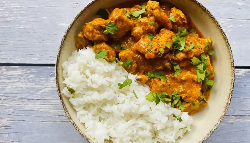 Aksamitny kurczak tikka masala w kremowym sosie, podany z puszystym ryżem i posypany świeżą kolendrą.